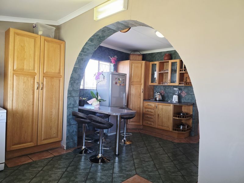 A kitchen featuring traditional wooden cabinetry, tiled flooring, and a distinctive arched entryway leading into the cooking and prep area.