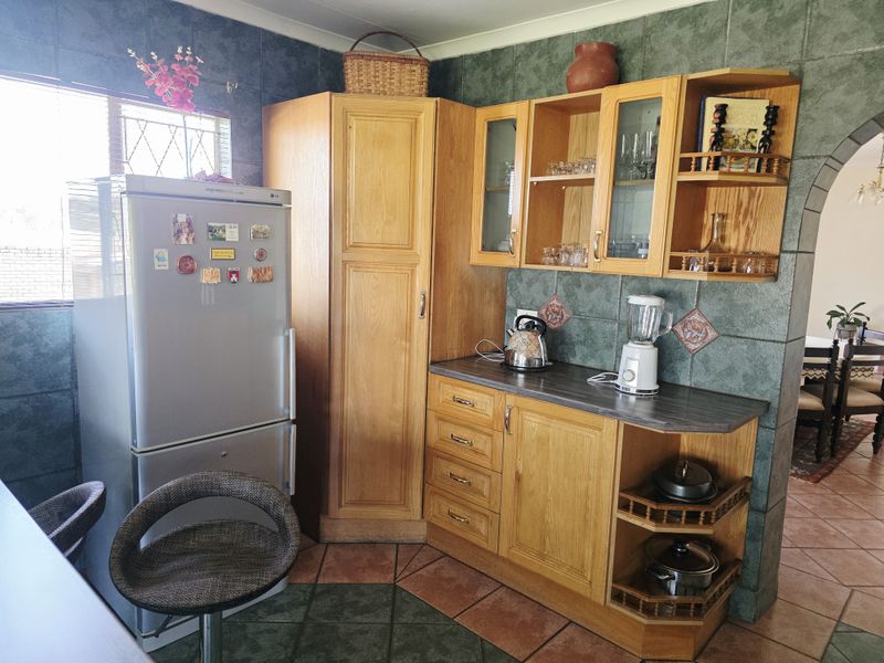 A kitchen area featuring traditional wooden cabinetry, dark tiled wall finishes, and tiled flooring, offering a functional layout with ample storage space.