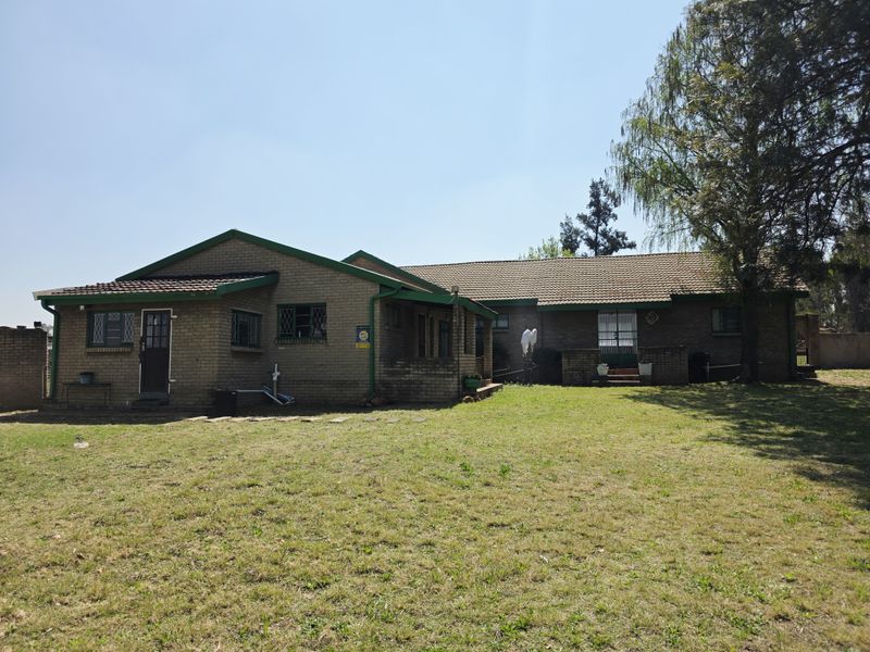 Rear view of a face-brick small holding residence featuring a tiled roof, security fixtures, and a spacious garden area.