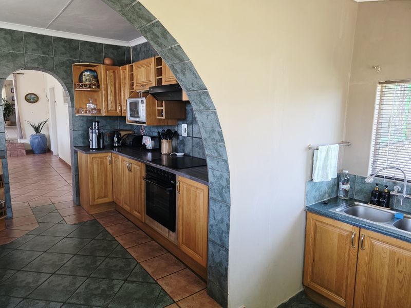 A functional kitchen featuring wooden cabinetry, built-in oven, electric hob, and tiled finishes, connected to the living area via a decorative archway.