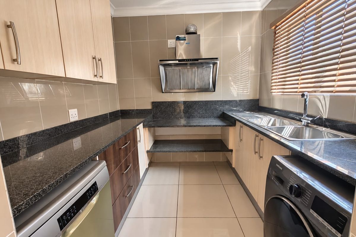 Modern kitchen featuring granite countertops, ample built-in cabinetry, a stainless steel extractor fan, and a double sink with tiled finishes.