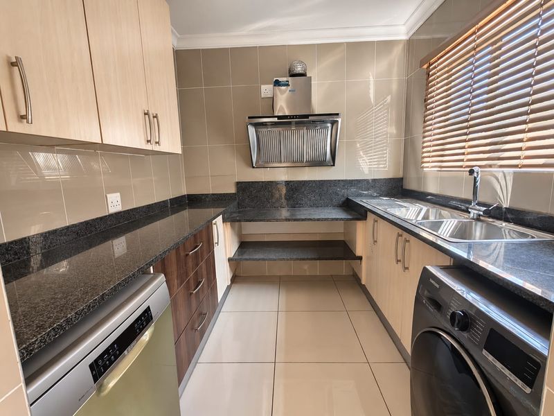 Modern kitchen featuring granite countertops, ample built-in cabinetry, a stainless steel extractor fan, and a double sink with tiled finishes.