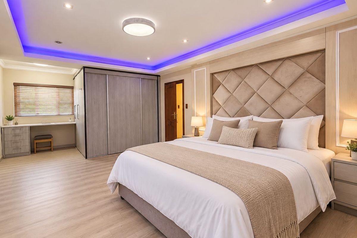 Spacious modern bedroom featuring a large built-in wardrobe, integrated desk area, and a stylish upholstered headboard with ambient recessed ceiling lighting.