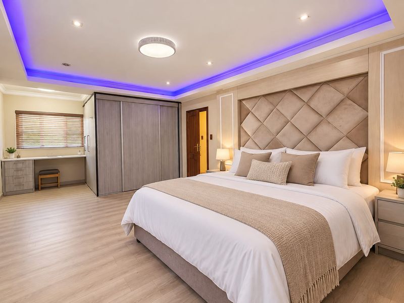 Spacious modern bedroom featuring a large built-in wardrobe, integrated desk area, and a stylish upholstered headboard with ambient recessed ceiling lighting.