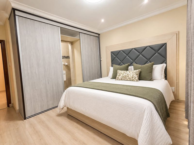 A well-maintained bedroom featuring modern laminate flooring, recessed lighting, and a large built-in sliding wardrobe with direct access to an en-suite bathroom.
