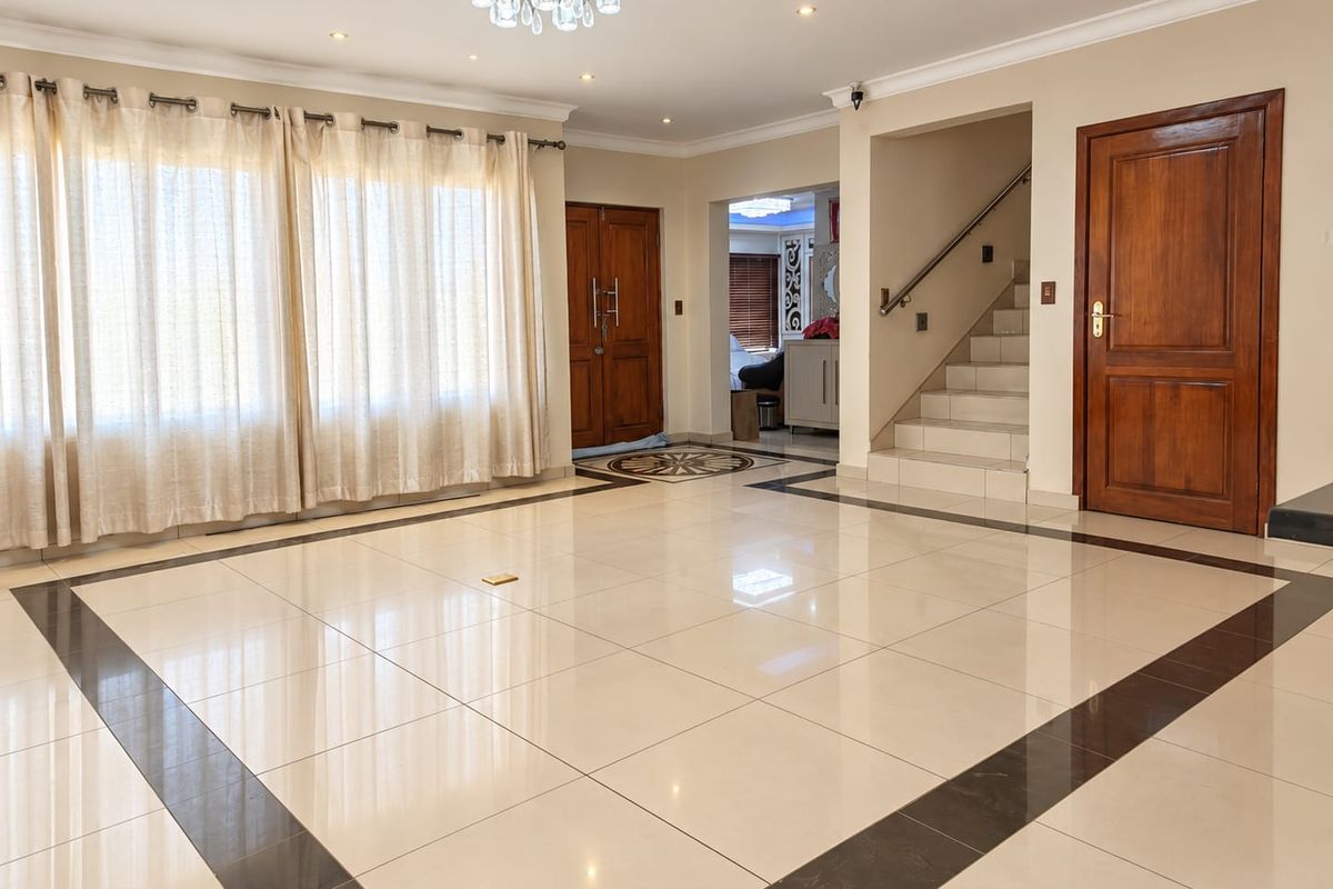 Spacious living area featuring polished porcelain tiles with decorative borders, recessed lighting, a central chandelier, and a staircase leading to the upper level.