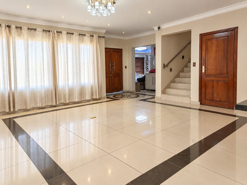 Spacious living area featuring polished porcelain tiles with decorative borders, recessed lighting, a central chandelier, and a staircase leading to the upper level.