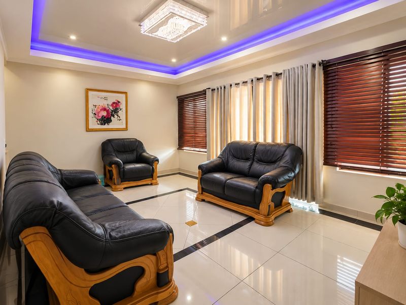 A well-maintained living room featuring polished porcelain floor tiles, a decorative recessed ceiling with integrated LED lighting, and a central crystal chandelier.
