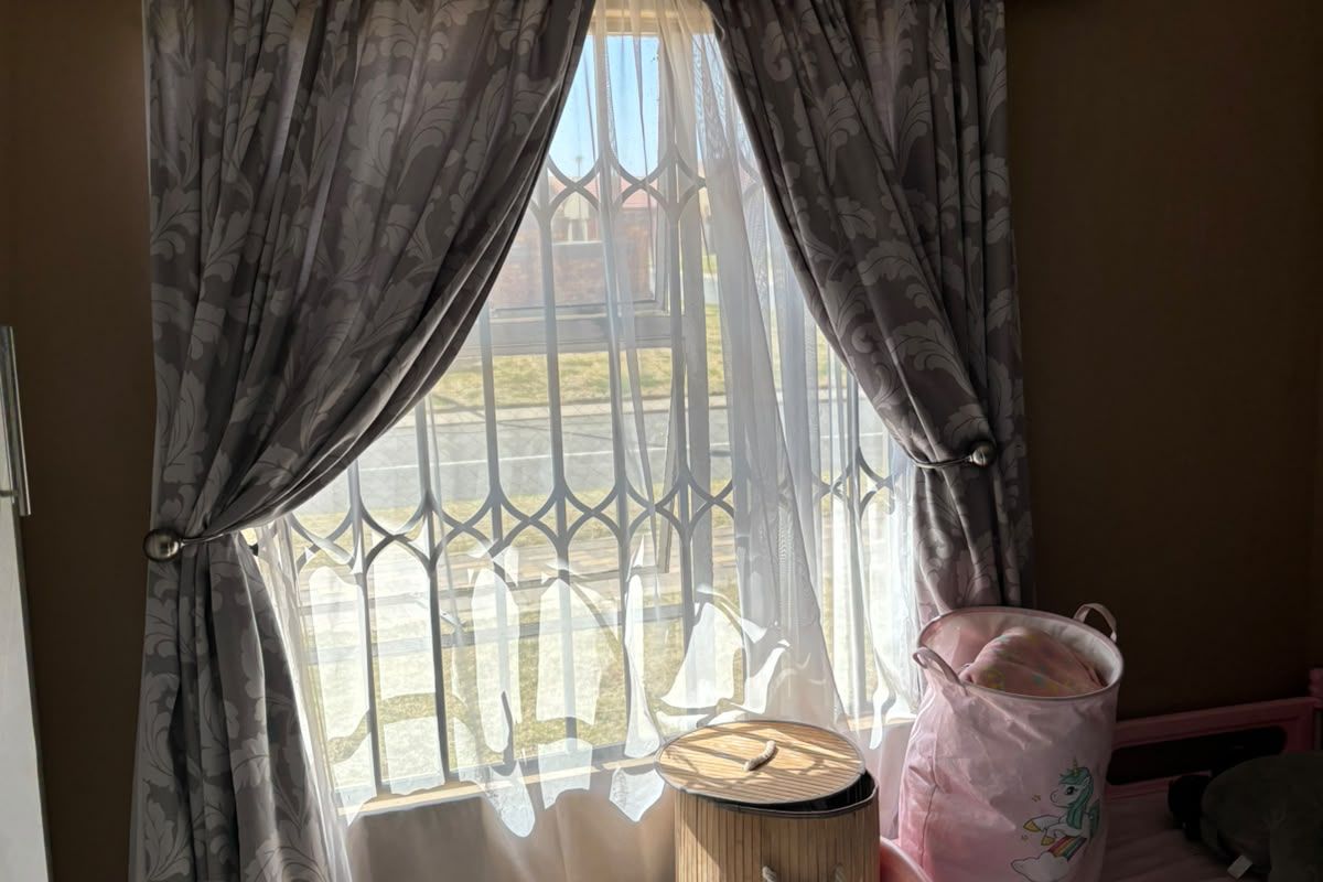 A bedroom featuring tiled flooring and a window fitted with a security gate and curtain rod.