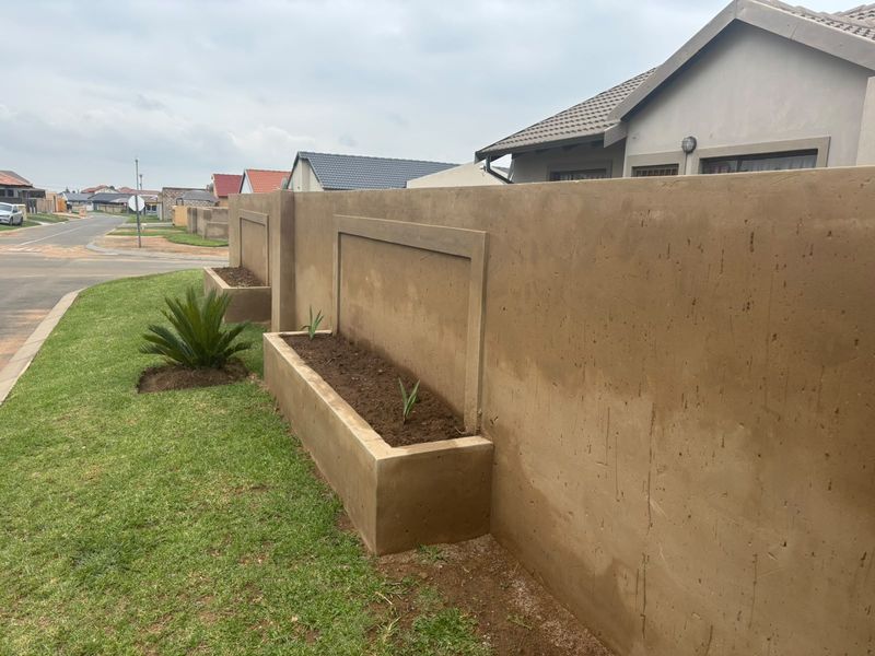 A view of the property's front boundary wall featuring integrated concrete planter boxes and a well-maintained lawn area.