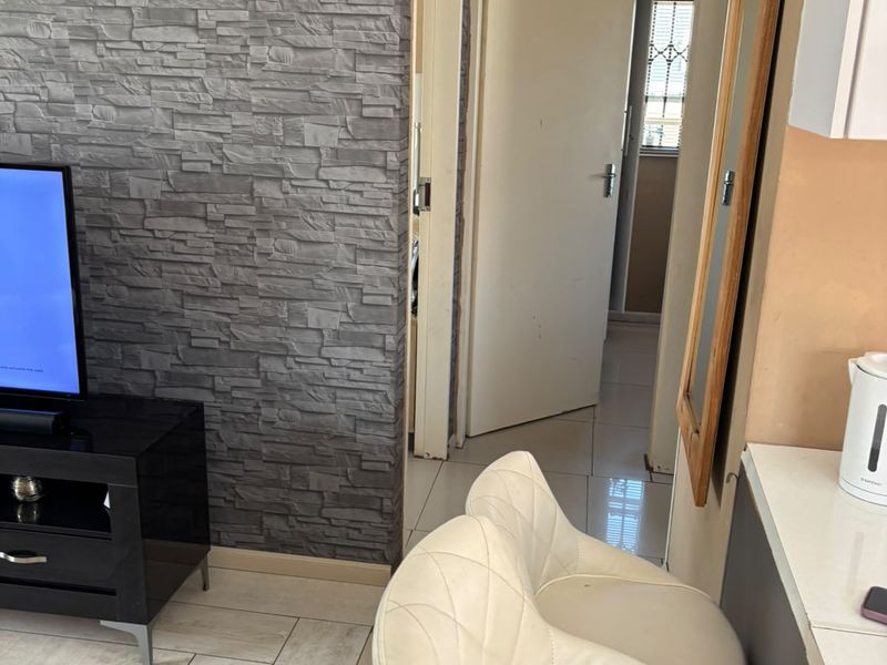 Open plan living area featuring a textured stone-cladding accent wall, tiled flooring, and a breakfast counter leading to a hallway.