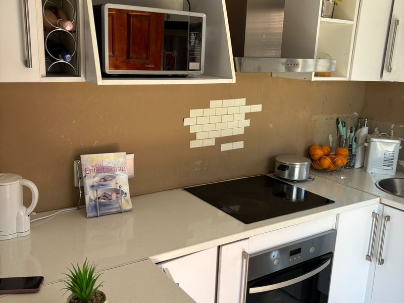 A functional kitchen featuring white cabinetry, stone countertops, a built-in oven, and an electric hob, with an incomplete tiled splashback area.