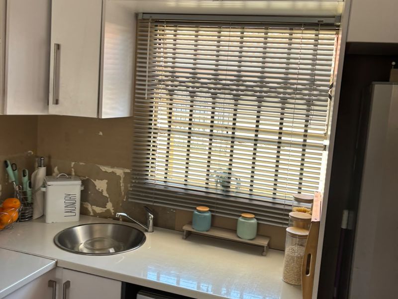 Compact laundry area featuring white built-in cabinetry, a stainless steel sink, and an integrated washing machine, requiring wall surface repairs.