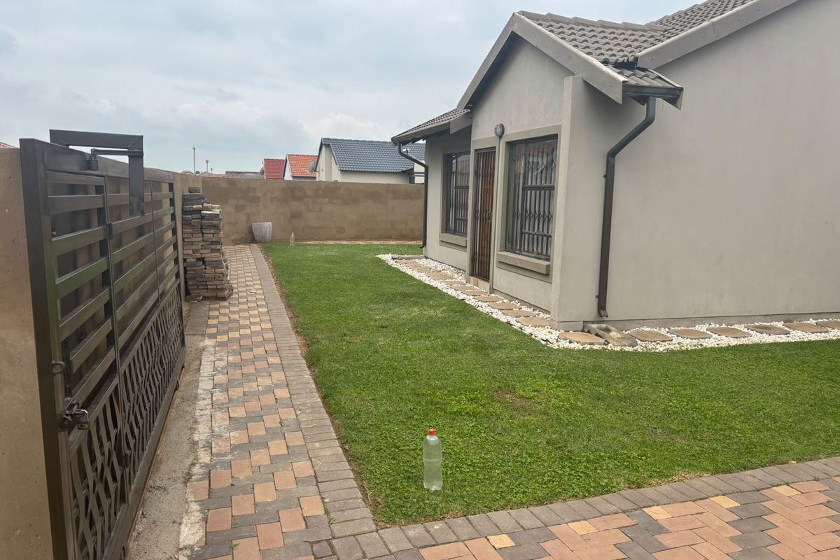 A view of the rear exterior of the house featuring a paved walkway, a small lawn, and a secure boundary wall.