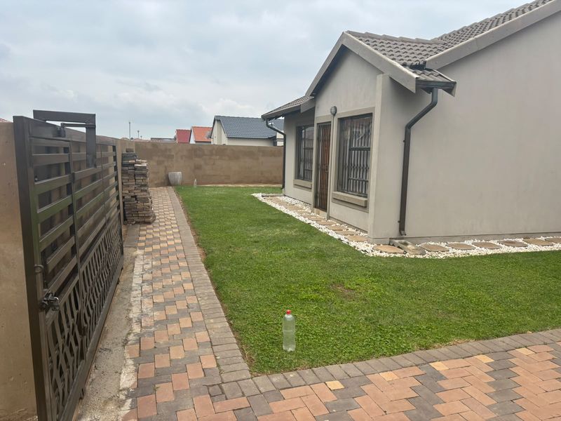A view of the rear exterior of the house featuring a paved walkway, a small lawn, and a secure boundary wall.