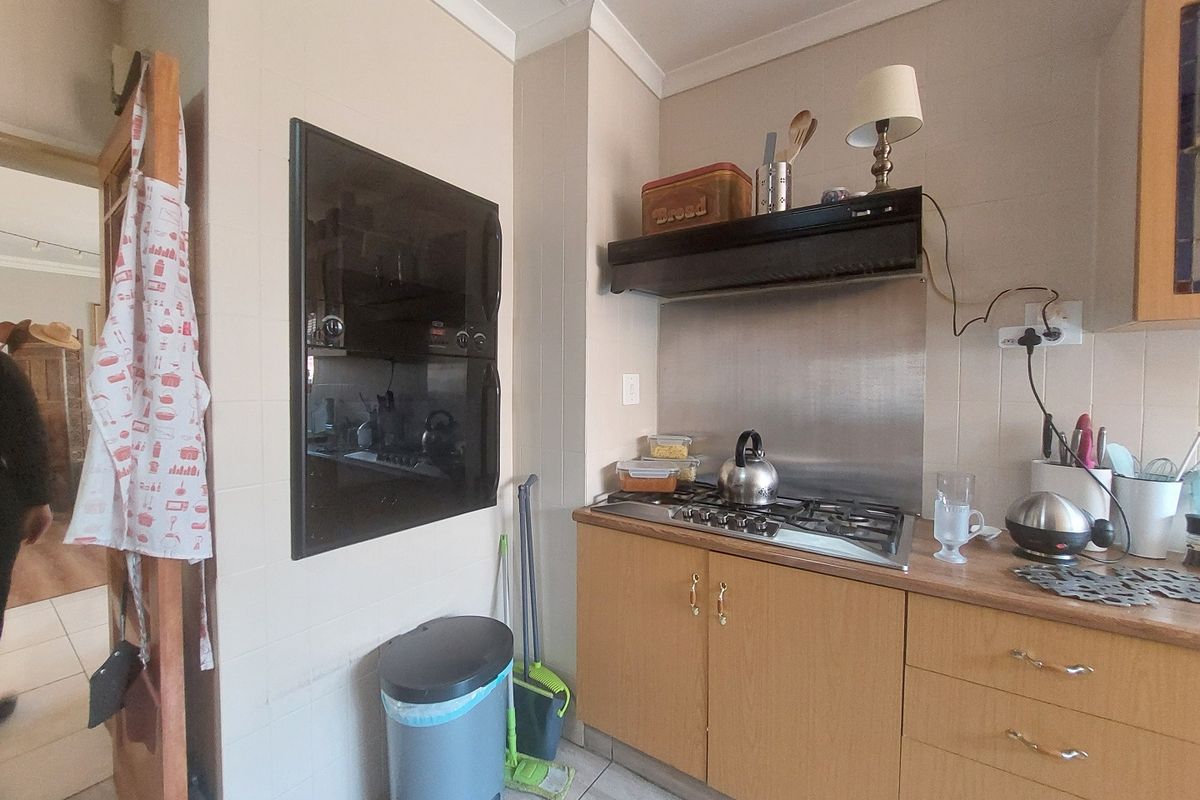 A functional kitchen area featuring a built-in oven, gas hob with extractor fan, and wood-look cabinetry with tiled splashbacks.