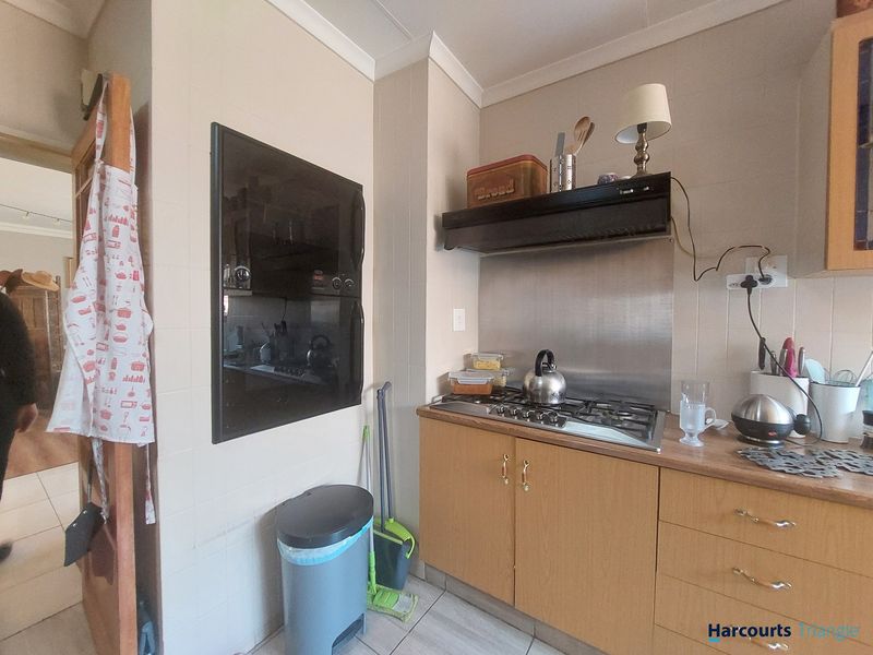 A functional kitchen area featuring a built-in oven, gas hob with extractor fan, and wood-look cabinetry with tiled splashbacks.