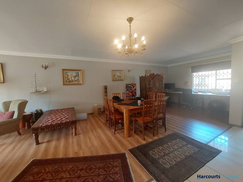 Spacious open-plan living and dining area featuring a mix of laminate and tiled flooring, illuminated by a classic chandelier.