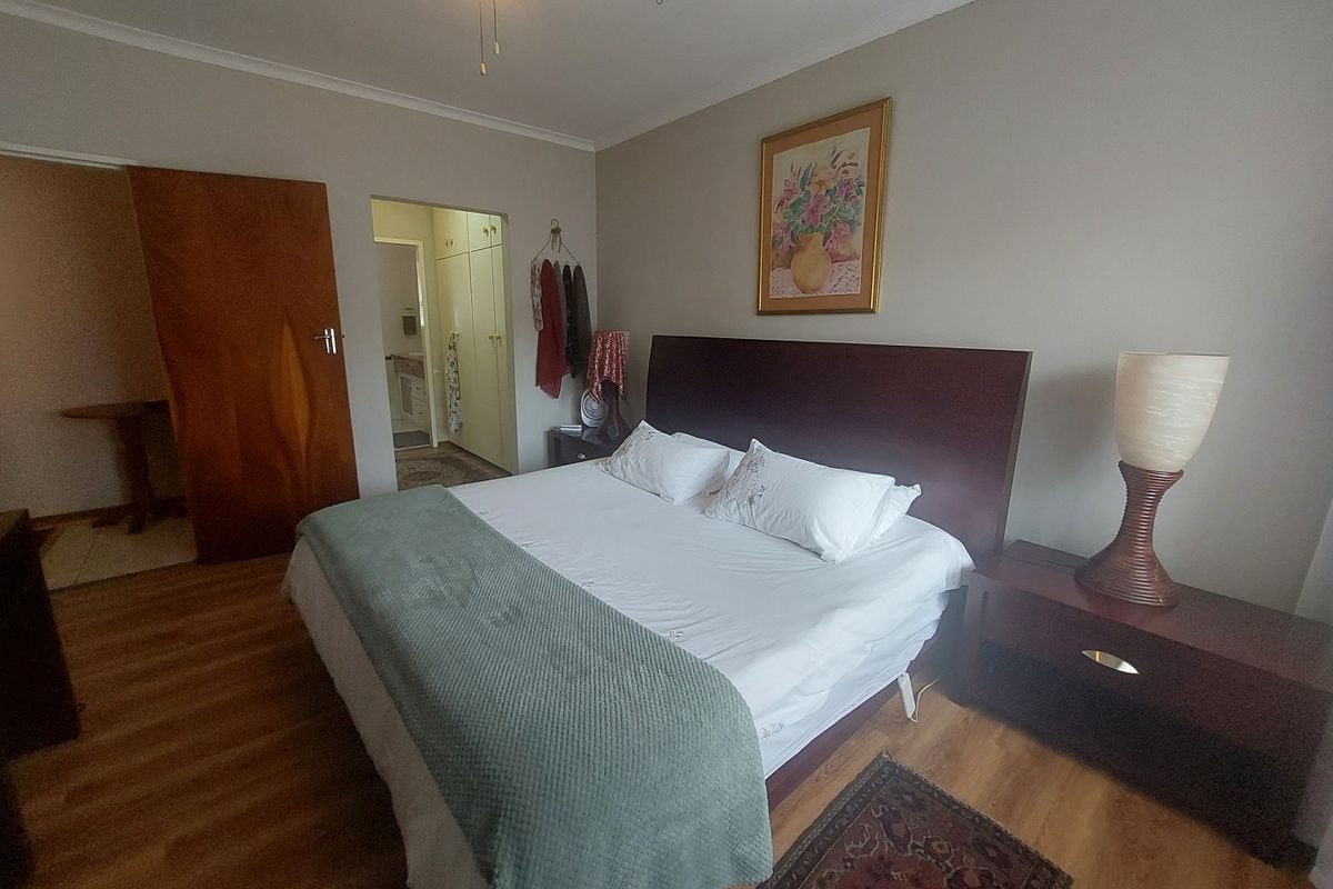 A well-proportioned bedroom featuring laminate flooring, a ceiling fan, and convenient access to an en-suite area with built-in storage.
