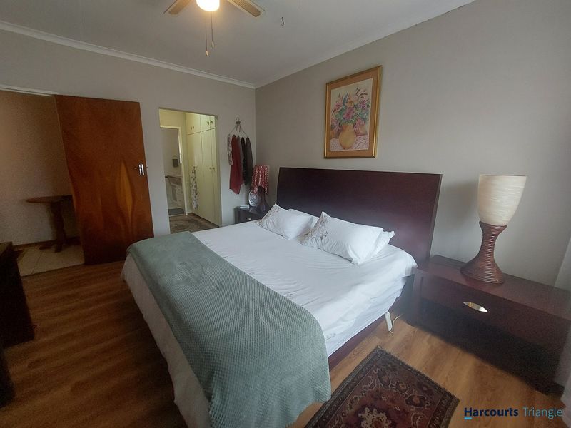 A well-proportioned bedroom featuring laminate flooring, a ceiling fan, and convenient access to an en-suite area with built-in storage.
