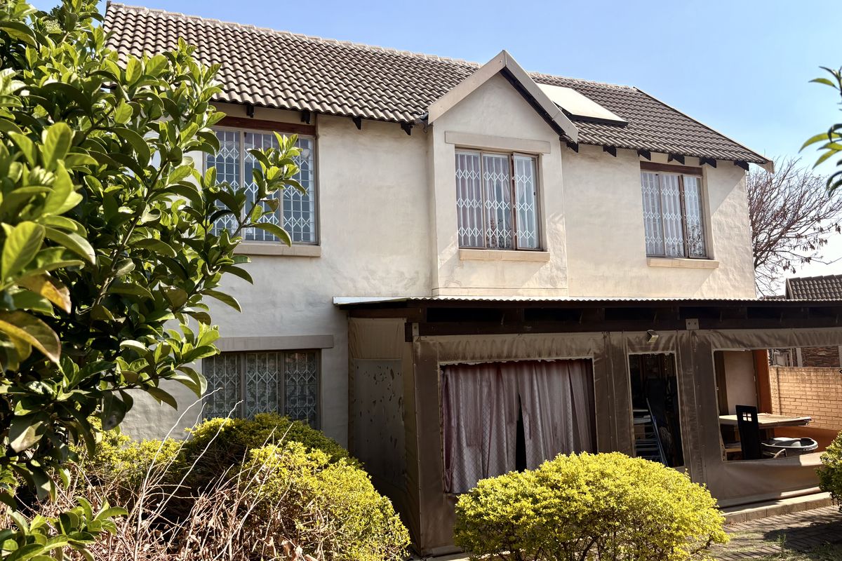 Rear view of a two-story townhouse featuring a tiled roof, security-barred windows, and a covered patio area with canvas enclosures.