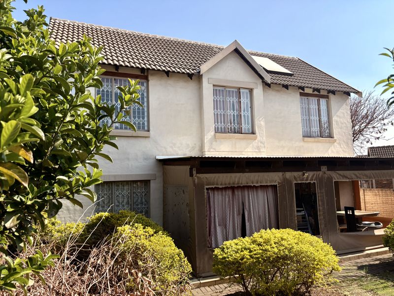 Rear view of a two-story townhouse featuring a tiled roof, security-barred windows, and a covered patio area with canvas enclosures.