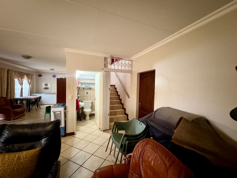 Open plan living area featuring tiled flooring, a staircase, and an adjacent ground floor bathroom with basic sanitary fixtures.