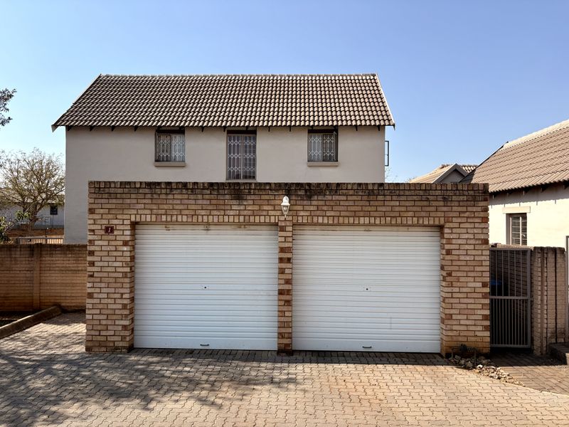 A double garage with roller doors and a brick facade, featuring a tiled roof and security bars on the upper-level windows.