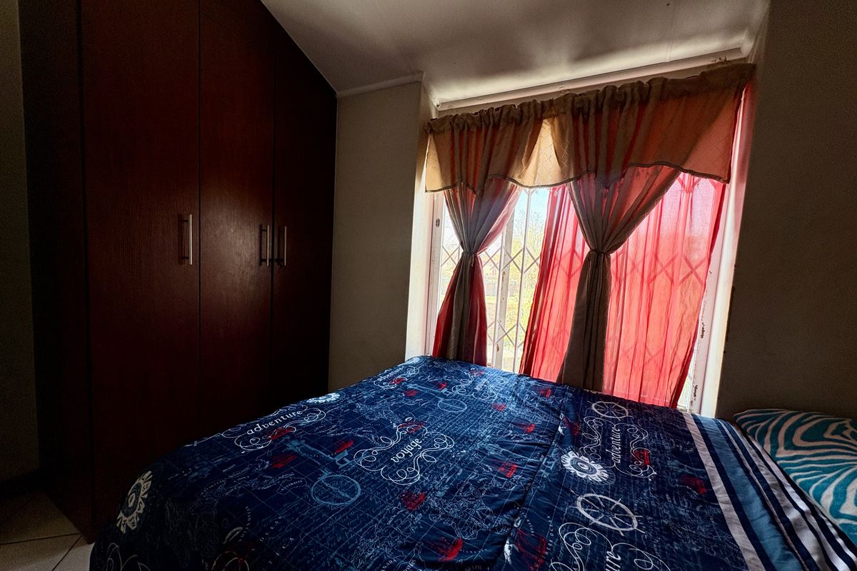 A bedroom featuring built-in wooden cupboards and a window fitted with a security gate.