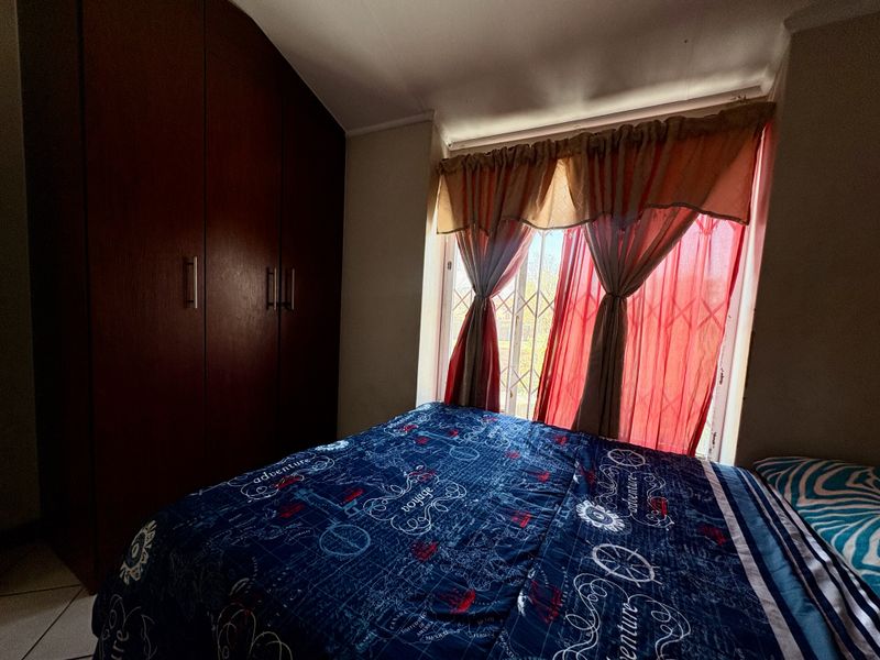 A bedroom featuring built-in wooden cupboards and a window fitted with a security gate.