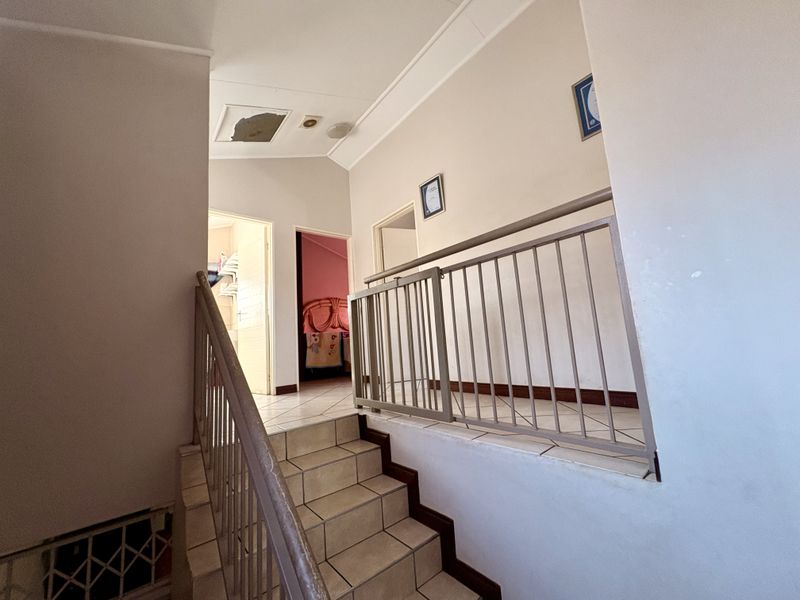 Upper level hallway featuring a tiled staircase with metal balustrade and access to adjacent bedrooms.