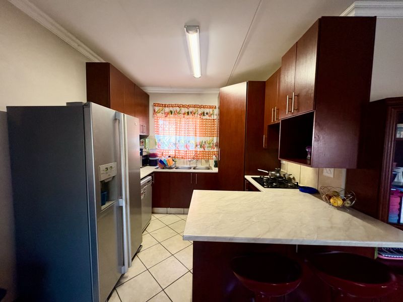 A functional kitchen featuring dark wood cabinetry, laminate countertops, a gas hob, and tiled flooring, offering a practical layout for daily meal preparation.