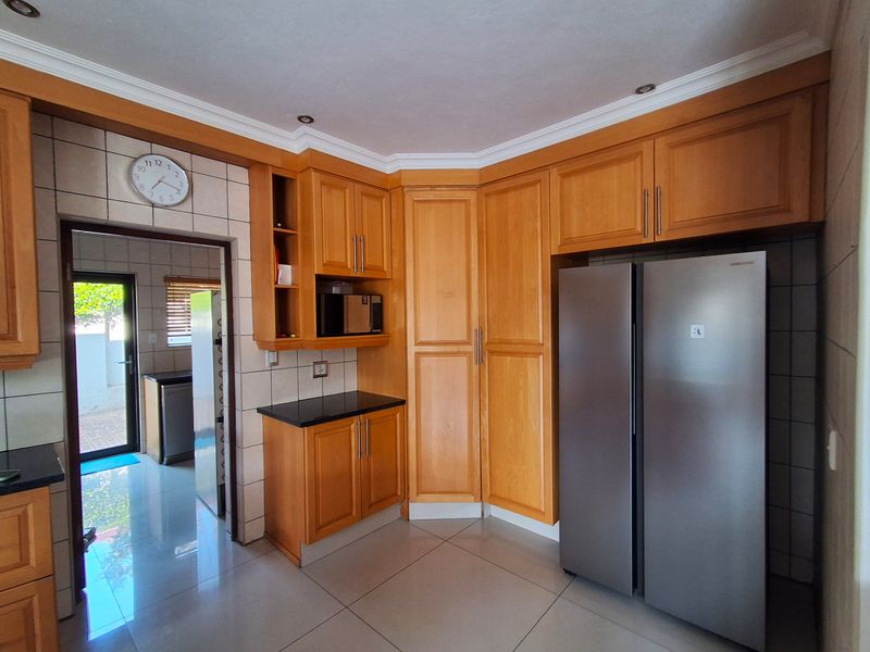 A well-maintained kitchen featuring warm wooden cabinetry, granite countertops, tiled flooring, and a functional layout with an adjacent scullery area.