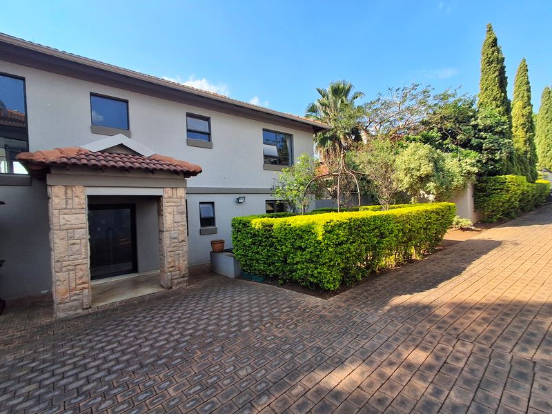 Front elevation of a two-story house featuring a stone-clad entrance porch, paved driveway, and well-maintained hedged garden.