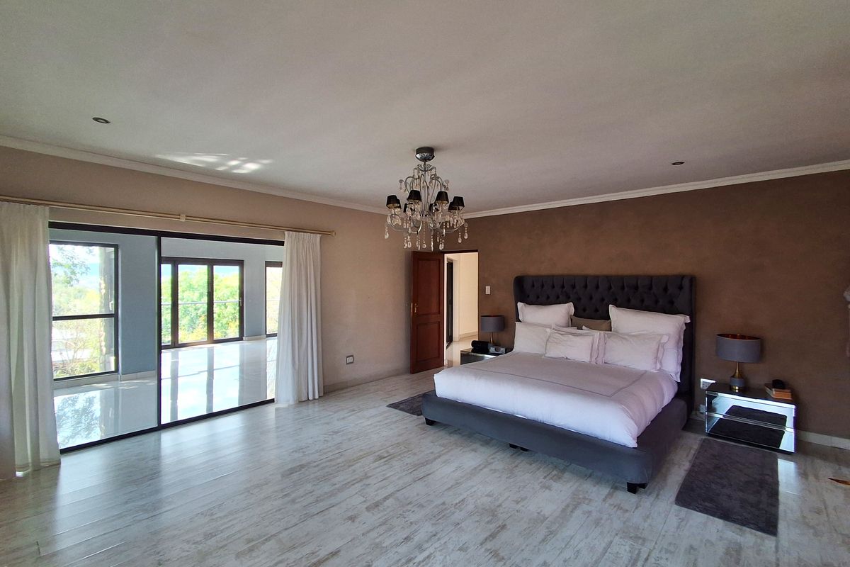 Spacious bedroom featuring tiled flooring, a decorative chandelier, and large sliding glass doors that open onto a balcony, providing ample natural light.