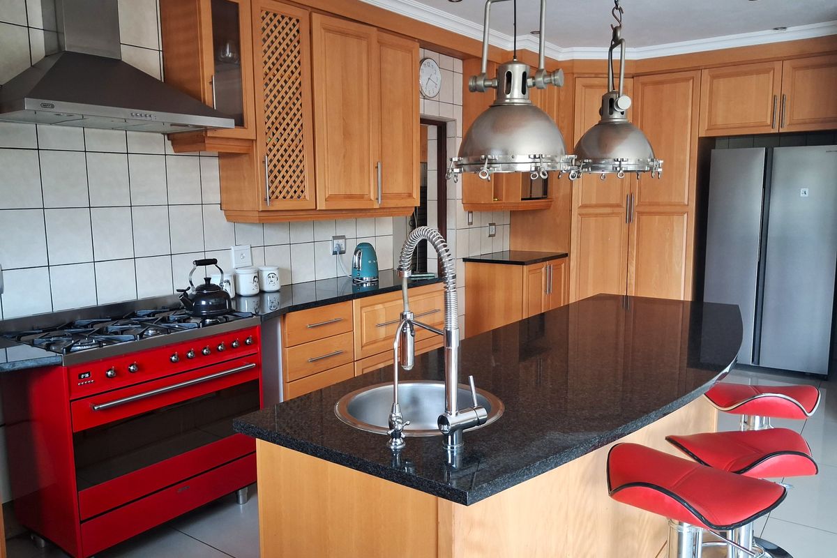A well-appointed kitchen featuring wooden cabinetry, granite countertops, a central island with a sink, and a prominent red gas stove.