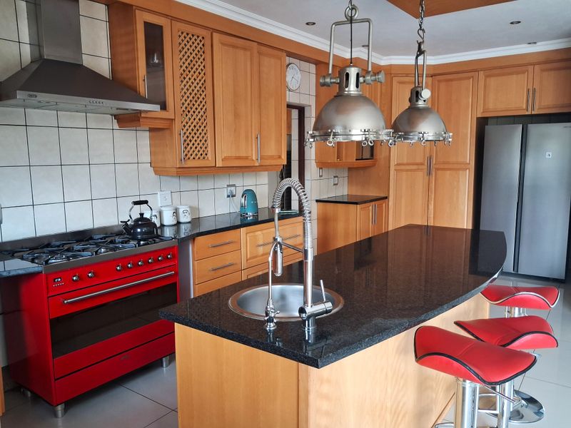 A well-appointed kitchen featuring wooden cabinetry, granite countertops, a central island with a sink, and a prominent red gas stove.