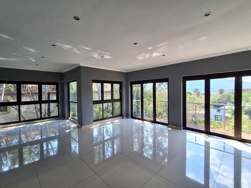 Spacious, light-filled living area featuring polished porcelain tiles, recessed lighting, and multiple glass sliding doors opening onto a balcony with scenic views.