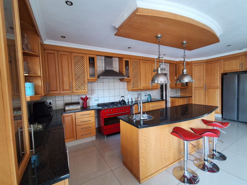 Spacious kitchen featuring warm wooden cabinetry, granite countertops, a central island with a prep sink, and a professional-style gas range with extractor hood.