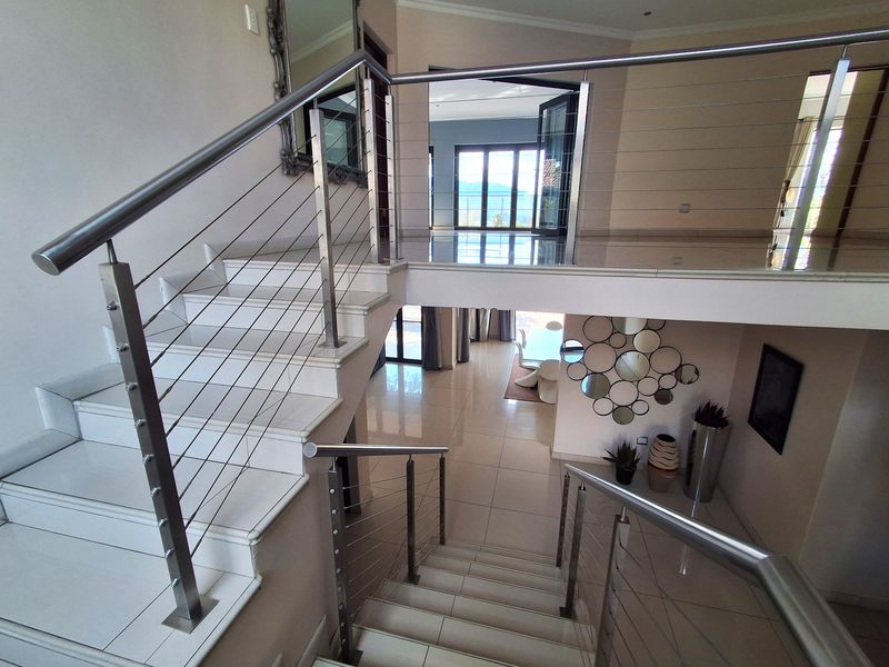 A bright, open-plan hallway featuring a modern staircase with stainless steel and wire cable balustrades, complemented by polished tiled flooring.