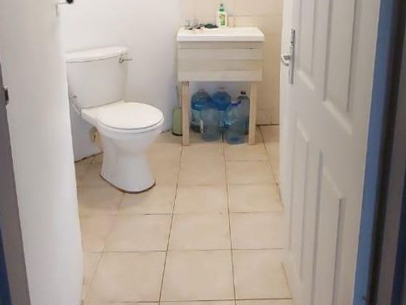 A functional bathroom featuring a standard toilet, pedestal sink, tiled flooring, and a louvre window, offering a basic layout ready for modernization.