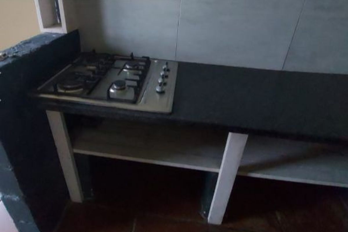 A basic kitchen prep area featuring a built-in gas hob, granite countertop, and open shelving with unfinished masonry elements.