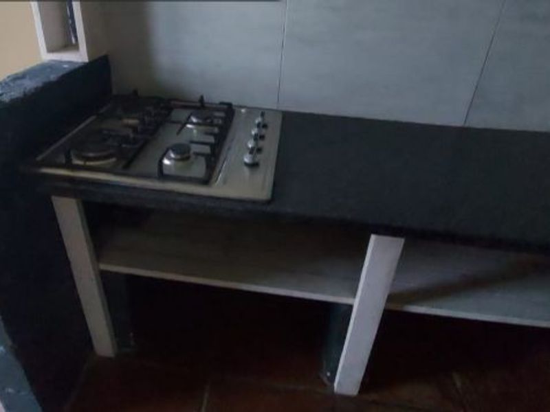 A basic kitchen prep area featuring a built-in gas hob, granite countertop, and open shelving with unfinished masonry elements.