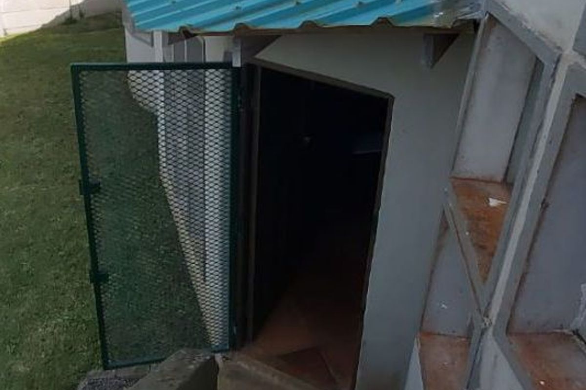 Rear exterior view showing concrete stairs leading to a side entrance with a corrugated metal roof and security gate.