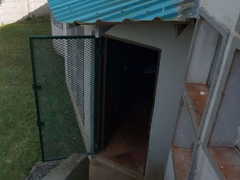 Rear exterior view showing concrete stairs leading to a side entrance with a corrugated metal roof and security gate.