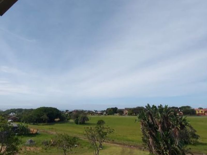 An elevated view overlooking a green landscape with surrounding residential properties and mature trees under a clear sky.