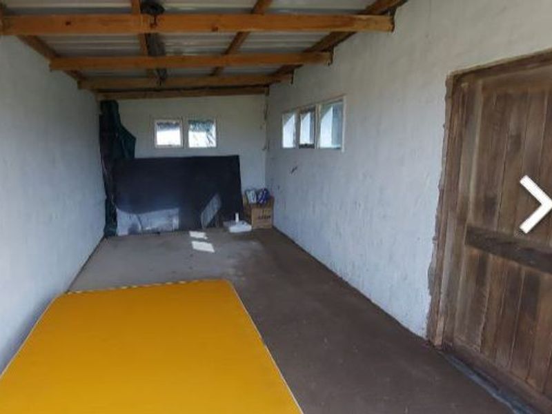 A basic utility space featuring exposed timber roof beams, concrete flooring, and a timber door, suitable for storage or workshop conversion.