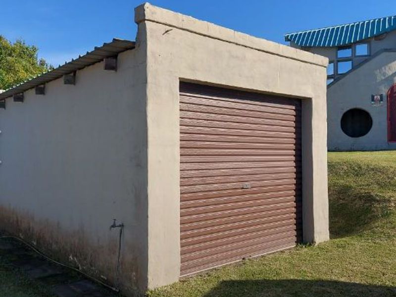 A detached single garage featuring a brown roller shutter door, corrugated metal roofing, and an external water tap.