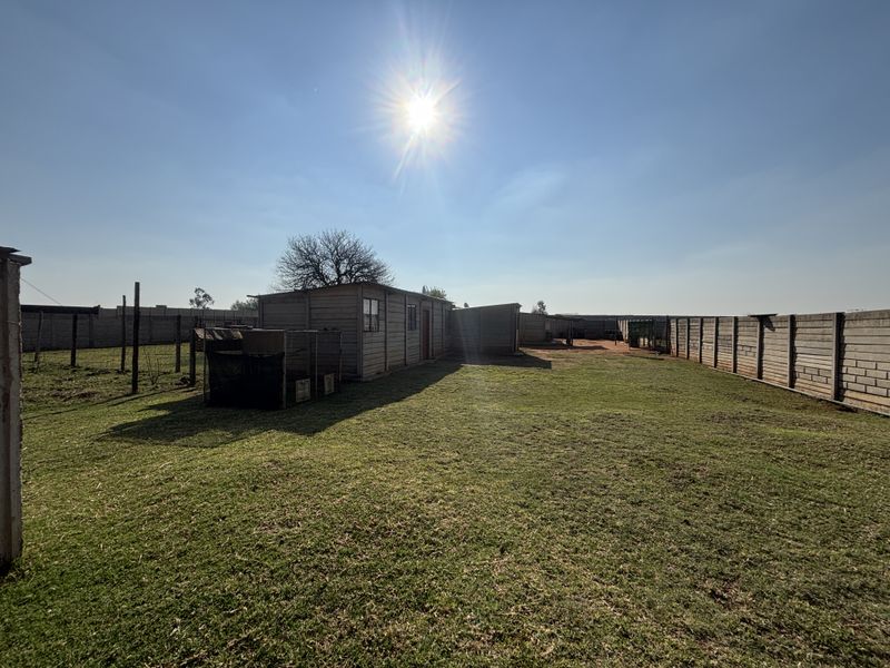 A wide-angle view of the rear yard featuring a large lawn, precast concrete boundary walls, and a functional outbuilding structure.