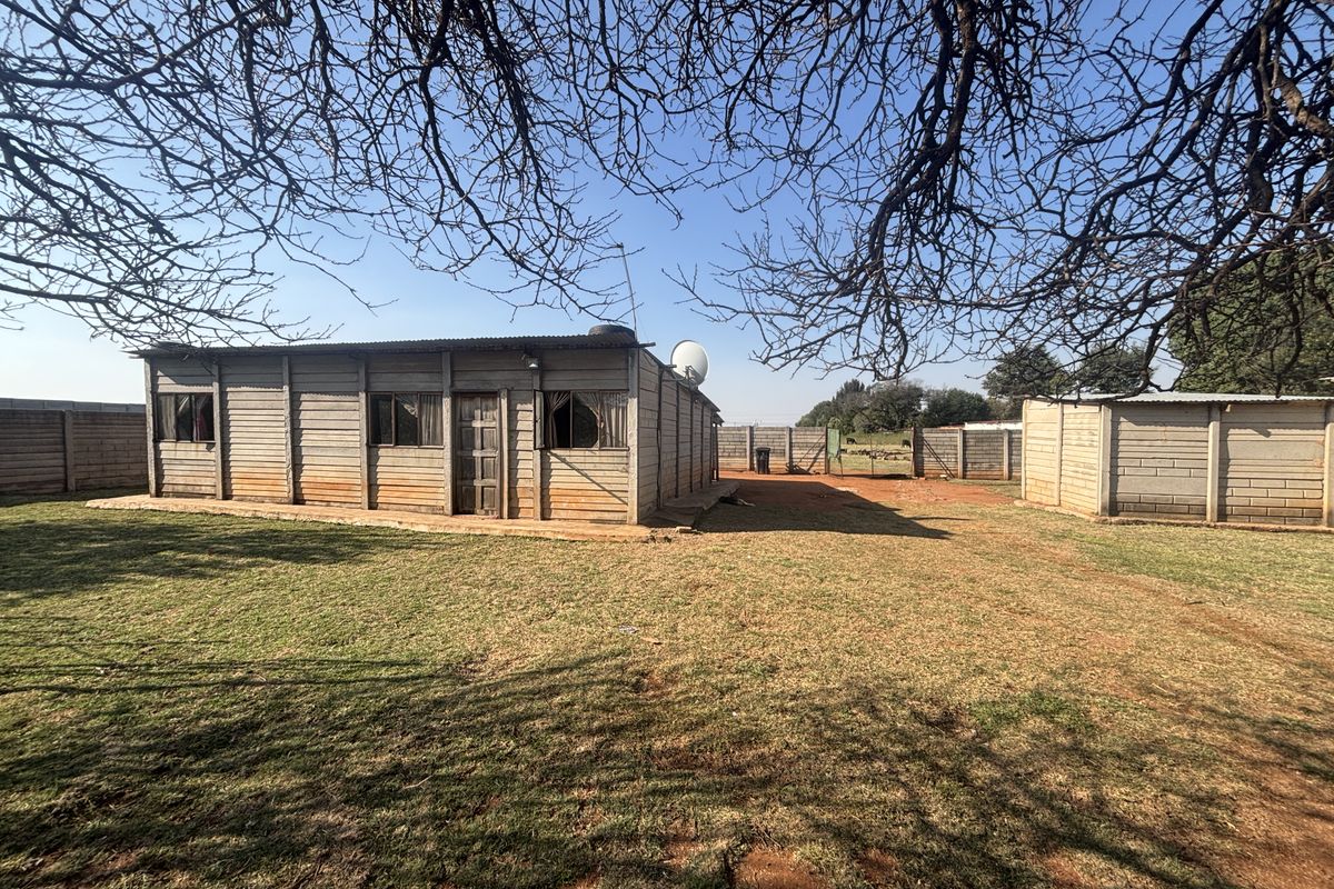 Rear view of a small holding property featuring a precast concrete structure, corrugated metal roofing, and surrounding perimeter walling on a large plot.
